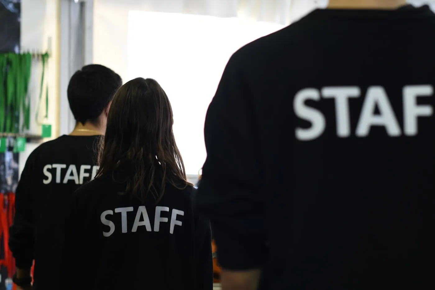 Pessoal de um evento, de costas, com casacos identificados como «staff».